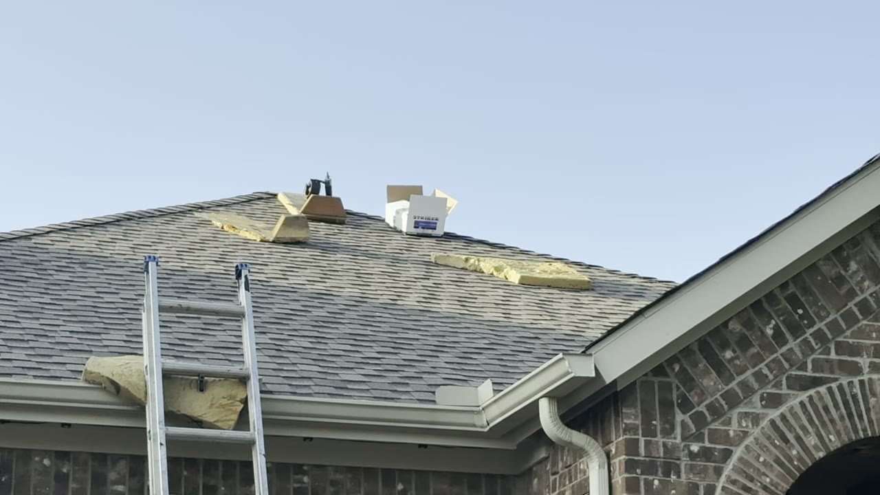 Ladder set against the gutter of a brick home with repair materials staged on the roof